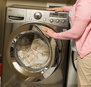 Woman loading sheets into home washing machine.