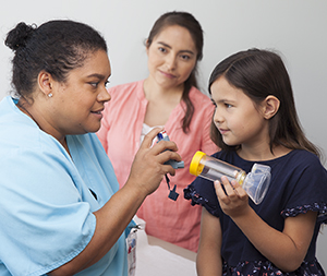 Proveedor de atención médica que les muestra a una mujer y a su hijo cómo usar un inhalador.