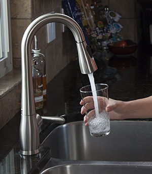 Primer plano de una mano llenando un vaso de agua en el fregadero de la cocina.