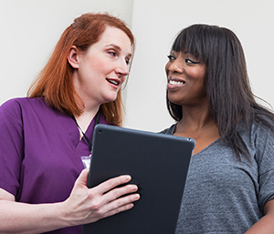 Un proveedor de atención médica que sostiene una tableta digital hablando con una mujer.