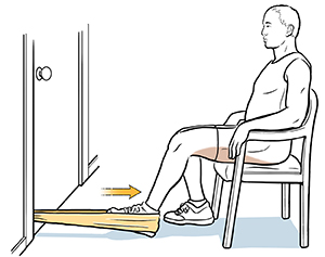 Un hombre sentado en una silla con el talón en una banda elástica hace un ejercicio de isquiotibiales.