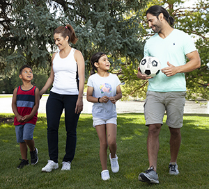 Hombre, mujer, niña y niño caminando en el parque con una pelota de fútbol.