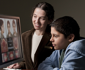 Proveedora de atención médica que muestra a un adolescente imágenes de sus dientes en un monitor de computadora.